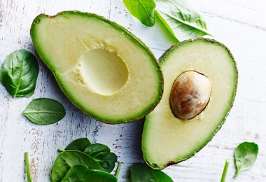 Palta partida por la mitad y hojas de espinaca alimentación balanceada Palta partida por la mitad y hojas de espinaca alimentación balanceada
