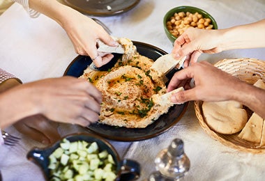 El hummus es tradicional en la comida libanesa. Un grupo de personas compartiendo hummus con pan pita, un clásico de la comida libanesa