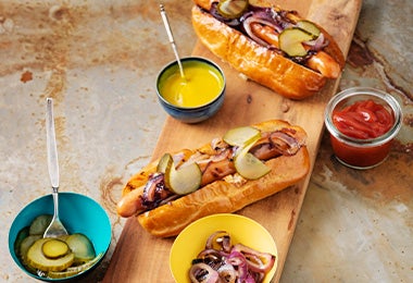 Tabla con hot dogs con salsas kétchup y mostaza Tabla con hot dogs con salsas kétchup y mostaza