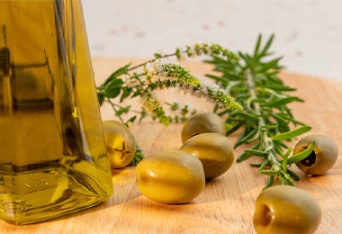 Aceite de oliva en un recipiente de vidrio acompañado de olivas y romero, un ingrediente ideal para conservar ensaladas