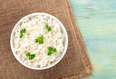 Arroz basmati en un tazón con hojitas de cilantro sobre un mantel café. 