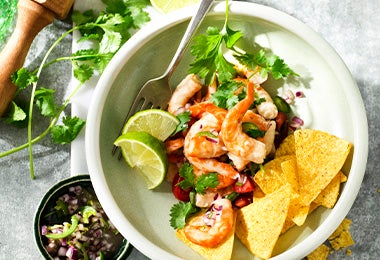 Camarones bañados en leche de tigre con nachos, hojas verdes y limón en toma cenital.