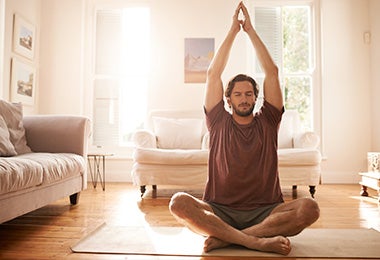 Hombre estirando para empezar a practicar yoga en casa con los ojos cerrados.
