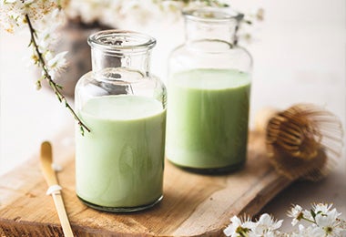 Matcha latté acompañado de unas flores blancas sobre una tabla, una de las bebidas calientes con leche más tradicionales que podés preparar