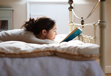 Mujer leyendo un libro en su cama antes de dormir para mejorar sus hábitos de sueño