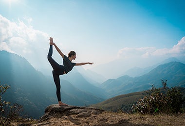 Mujer sobre una roca haciendo una postura de yoga con solo una pierna de apoyo