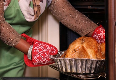 Mujer sacando pollo del horno utilizando guantes y agarraderas de cocina