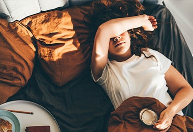 Una mujer en su cama con una taza y equilibrando sus hábitos de sueño