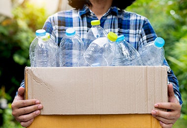 Persona cargando caja con botellas de agua vacías para reciclarlas