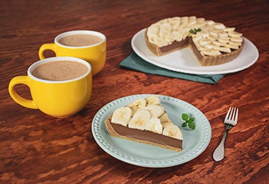 Porción de pie de chocolate con banano con dos tazas de chocolate