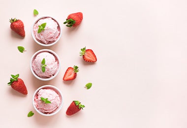 Tres vasos de helado decorados con hojas y rodeados de frutillas frescas es un postre sin gluten ideal