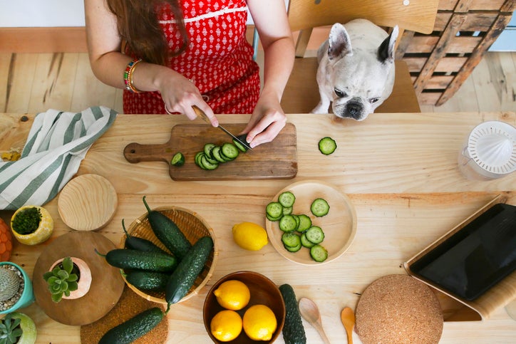 Mujer cortando pepino con la técnica rondelle en una mesa llena de ingredientes.