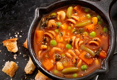 Sopa de pasta y verduras preparada en una olla de hierro. 