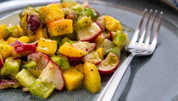 Una ensalada con mango y verduras, con su aderezo. 