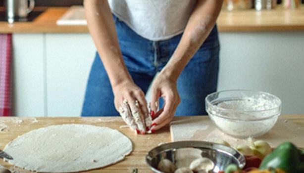 Mujer con utensilios e ingredientes preparando masa para pizza
