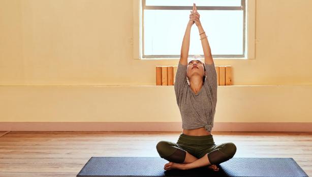 Mujer practicando yoga en casa encima de una esterilla y con los brazos estirados hacia arriba