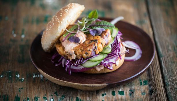 Apetitosa hamburguesa de pescado con vegetales emplatada y sobre una mesa de madera
