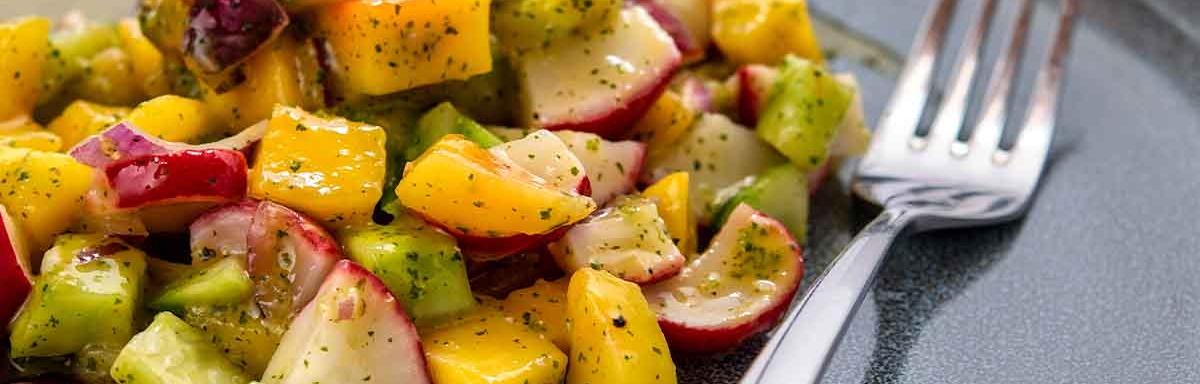 Una ensalada con mango y verduras, con su aderezo. 