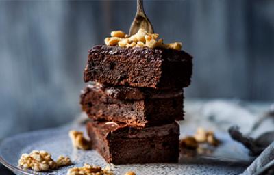 Plato con tres pisos de brownie espolvoreado con nueces, este es un postre sin gluten Plato con tres pisos de brownie espolvoreado con nueces, este es un postre sin gluten
