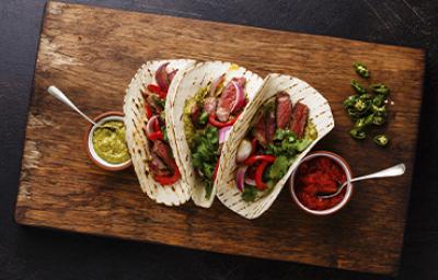 Tacos con jalapeños y ají casero sobre una tabla y un fondo negro Tacos con jalapeños y ají casero sobre una tabla y un fondo negro