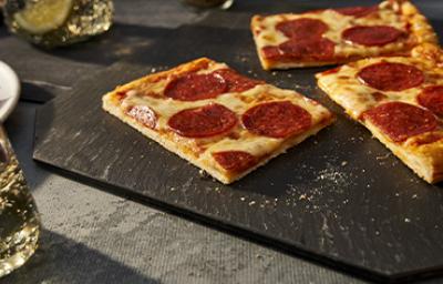 Porción de pizza de pepperoni con una masa delgada sobre un plato negro para celebrar su Día Mundial Porción de pizza de pepperoni con una masa delgada sobre un plato negro para celebrar su Día Mundial