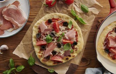 Mesa con pizza de prosciutto con aceitunas, tomates y rúcula Mesa con pizza de prosciutto con aceitunas, tomates y rúcula