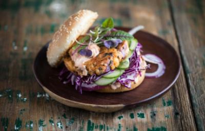 Apetitosa hamburguesa de pescado con vegetales emplatada y sobre una mesa de madera