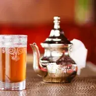 Bebida fermentada sin alcohol servida en una copa de vidrio y acompañada de una tetera de plata
