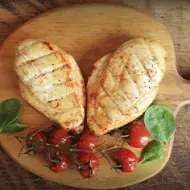 Dos pechugas de pollo con un racimo de tomates cherry, una comida con proteínas magras encima de una tabla