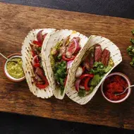 Tacos con jalapeños y ají casero sobre una tabla y un fondo negro