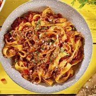 Pasta a la boloñesa con carne, queso parmesano y hierbas aromáticas sobre un fondo amarillo