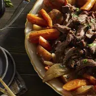 Carne de cabrito asado sobre cama de vegetales y papas