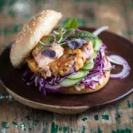 Apetitosa hamburguesa de pescado con vegetales emplatada y sobre una mesa de madera