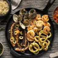 Sartén de hierro fundido con pulpo a la parrilla y variedad de mariscos