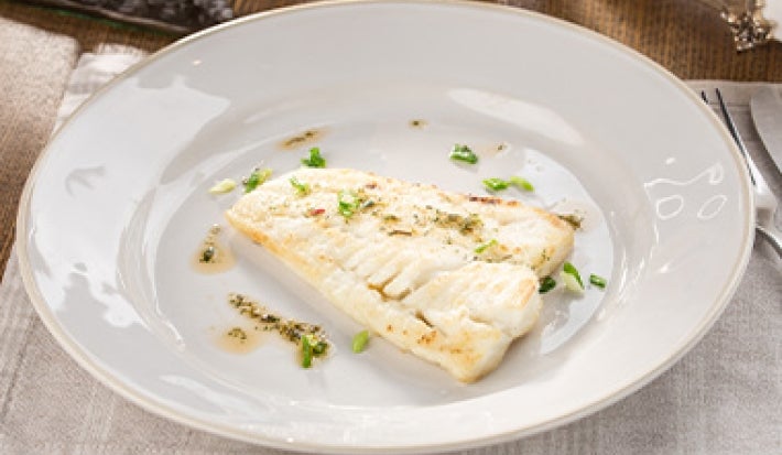 Un pescado cocinado al vapor en un plato blanco.