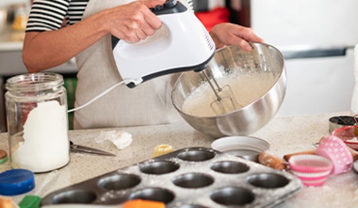Mujer mezclando masa de muffins frente a una mesa con moldes de silicona. Mujer mezclando masa de muffins frente a una mesa con moldes de silicona.