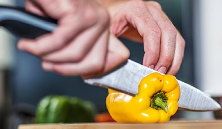 Un cuchillo con buen filo no puede faltar en un asado. Una persona cortando un morrón con un cuchillo, un utensilio clave para un asado.