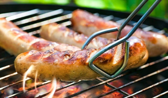 Las salchichas y las pinzas no pueden faltar en un asado Salchichas a la parrilla, con pinzas para darles vuelta.